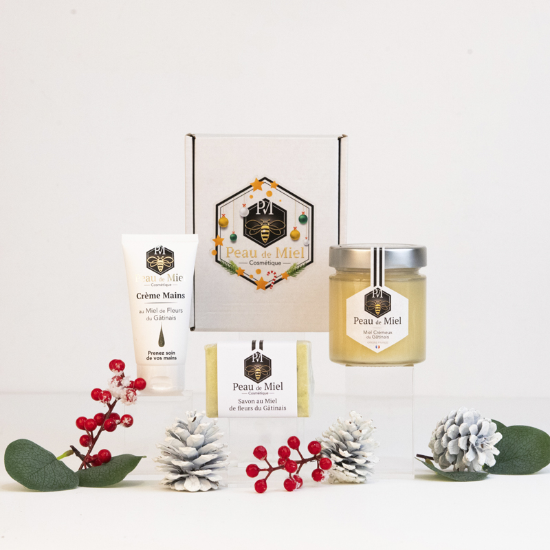 Une collection délicatement arrangée de produits cosmétiques Peau de Miel, comprenant un pot de miel d'été doré récolté, un savon au miel artisanal, un shampoing enrichi en miel et une crème pour les mains apaisante, présentée dans un coffret cadeau élégant, prête à ravir les amateurs de soins naturels pour Noël
