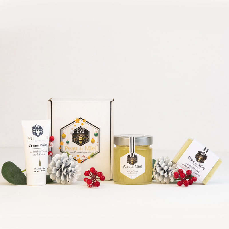 Un coffret cadeau Peau de Miel élégamment emballé, comprenant un pot de miel dorées, une crème pour les mains hydratante et des savons naturels aux teintes douces.