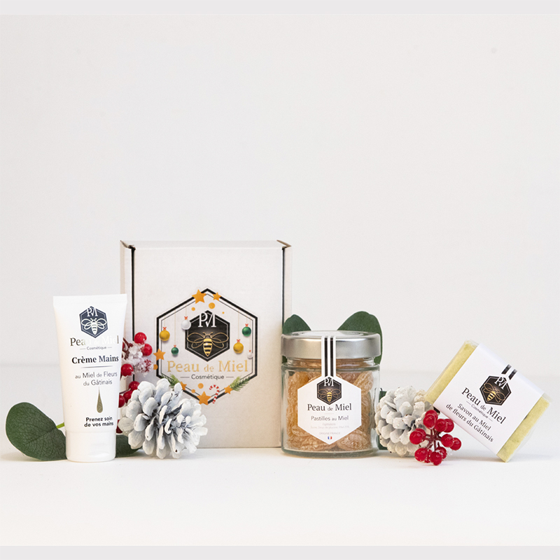 Un coffret cadeau Peau de Miel élégamment emballé, comprenant des pastilles de miel dorées, une crème pour les mains hydratante et des savons naturels aux teintes douces